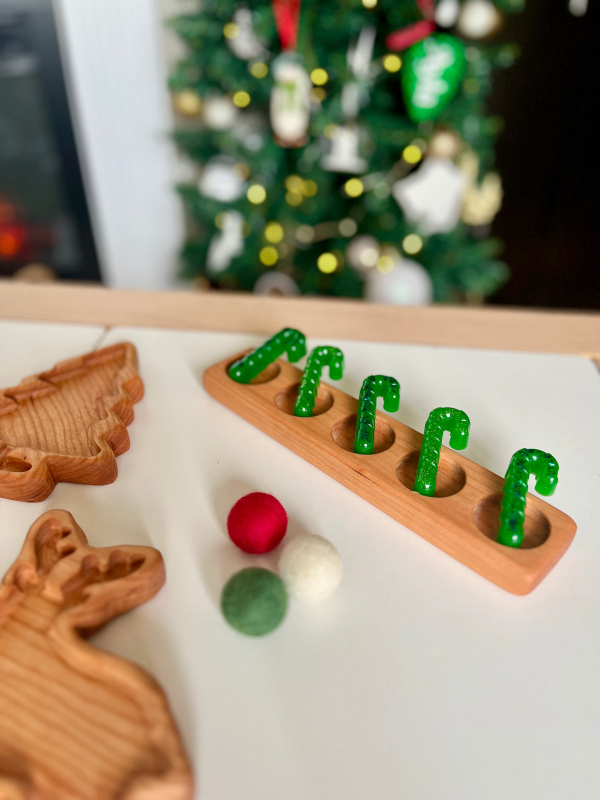 Wooden toy with five green candy cane pegs in a row, alongside felt balls and wooden holiday-shaped trays