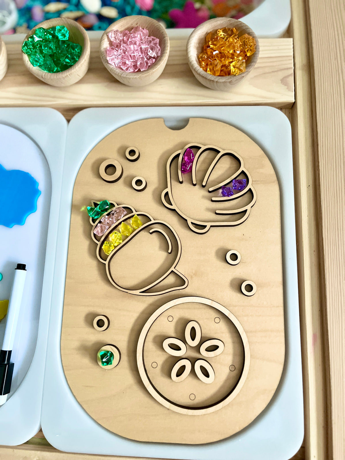 Wooden board with shell and acorn shapes filled with colorful translucent gem beads and small wooden rings