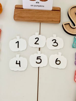 Set of six white pumpkin-shaped dry erase boards numbered 1 to 6 with wooden card holder on white surface