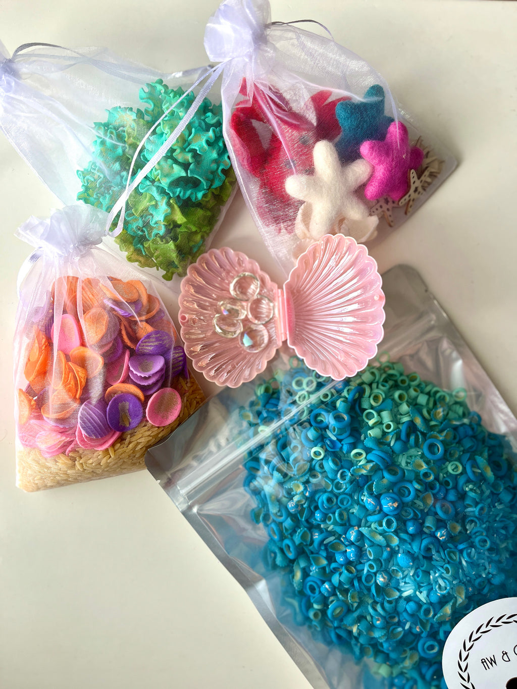 Organza bags with colorful felt sea creatures, green coral pieces, orange shells, and blue ring beads with a pink shell container.