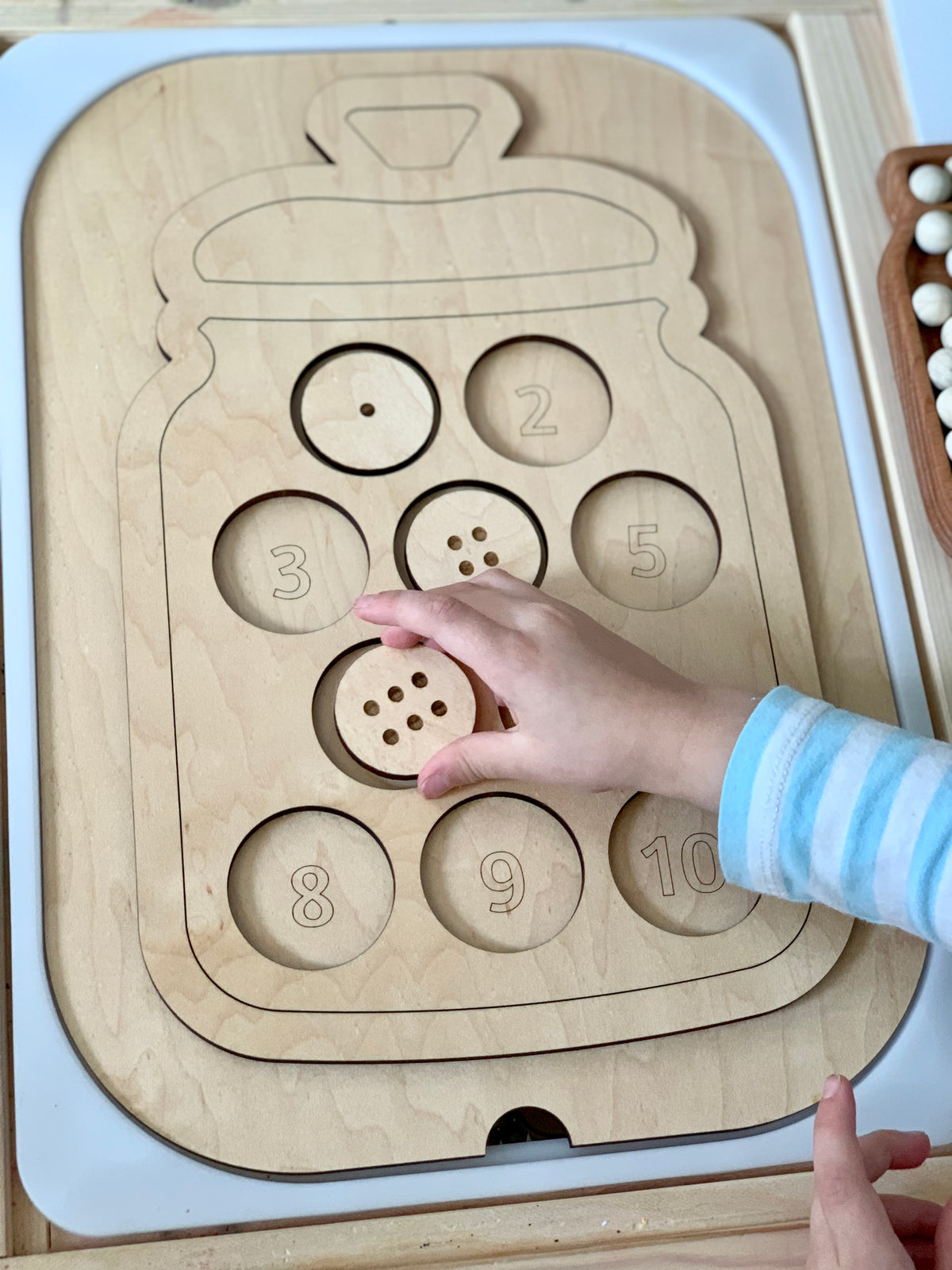 Wooden jar-shaped Flisat table insert with number-labeled cookie slots and child placing a wooden cookie piece