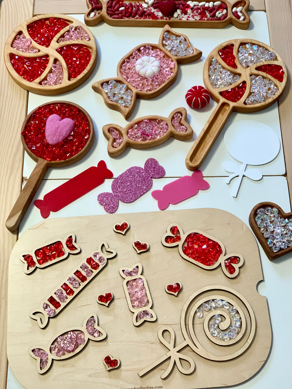 Wooden trays and shaped cutouts filled with red, pink, and clear acrylic beads arranged on a light surface