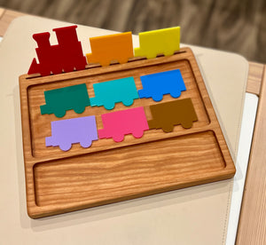 Wooden puzzle tray with colorful painted train engine and seven train car pieces in various bright colors on a table surface