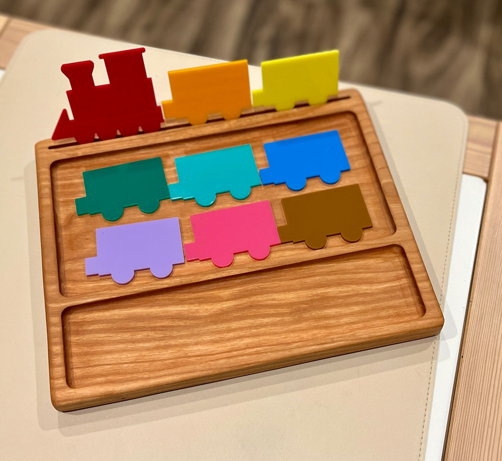 Wooden puzzle tray with colorful painted train engine and seven train car pieces in various bright colors on a table surface