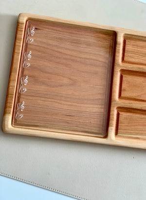 Wooden organizer tray with engraved musical staff lines and clefs on left section and small rectangular compartments on right side