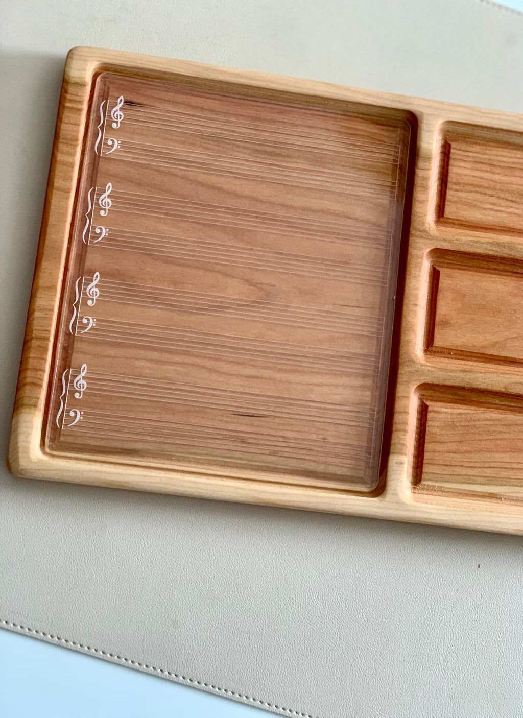 Wooden organizer tray with engraved musical staff lines and clefs on left section and small rectangular compartments on right side