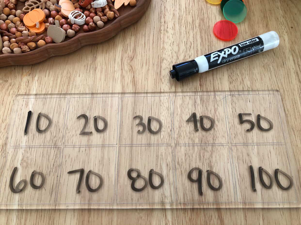 Clear plastic board divided into ten sections with numbers 10 to 100 written on each square and dry erase marker nearby