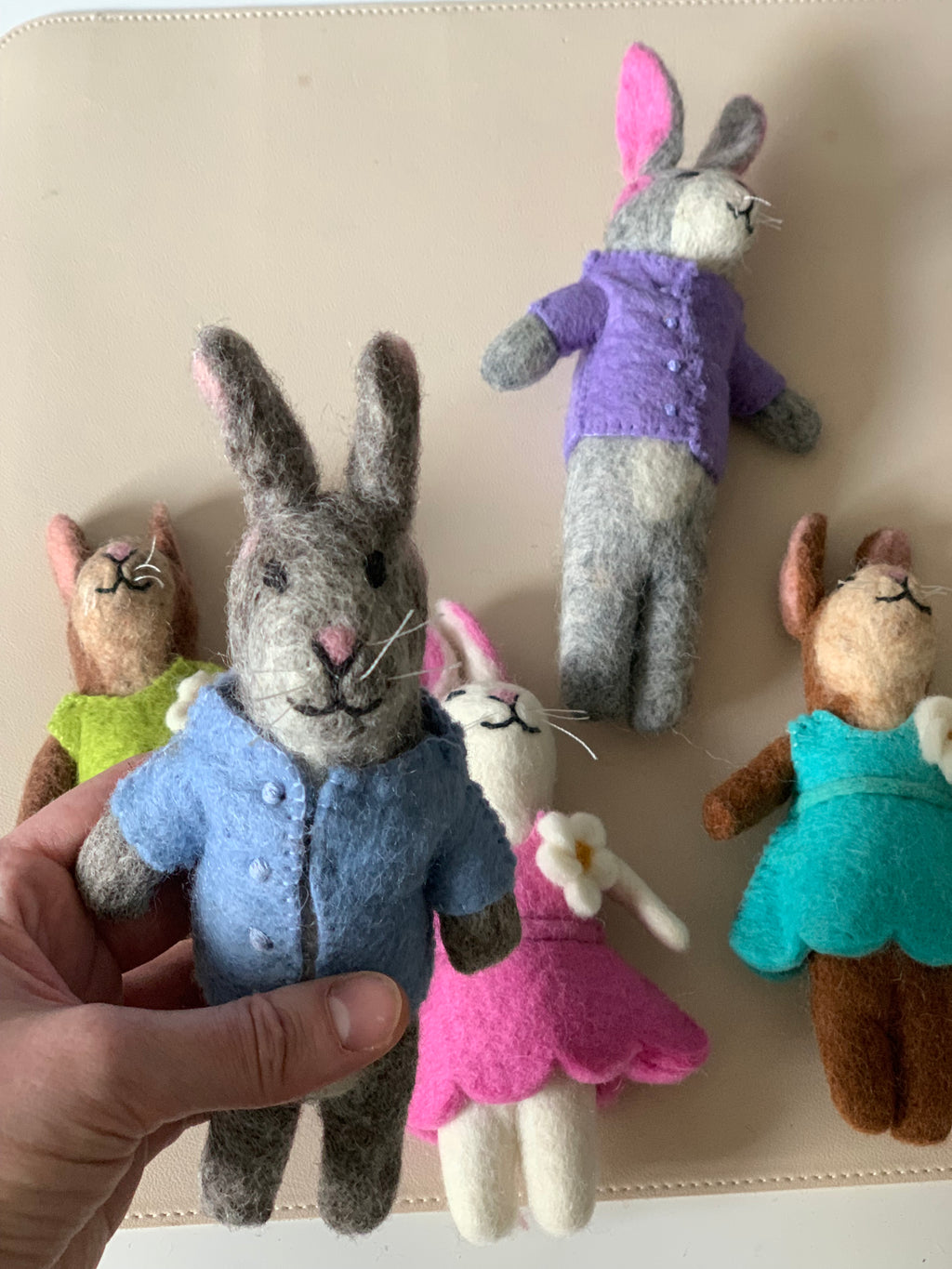Handmade felt bunny dolls in colorful clothes with one held in hand on a beige surface