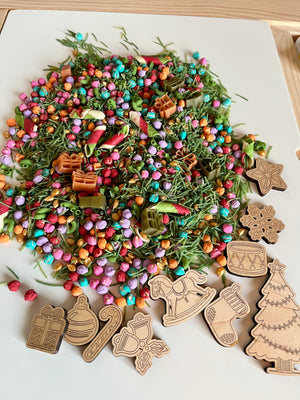 Colorful sensory mix of beads, dried botanicals, pasta, and wooden Christmas-themed cutouts on white surface