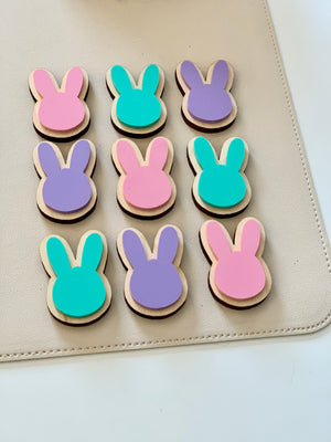 Set of pastel pink, purple, and teal wooden bunny-shaped cookies on beige surface arranged in a grid pattern
