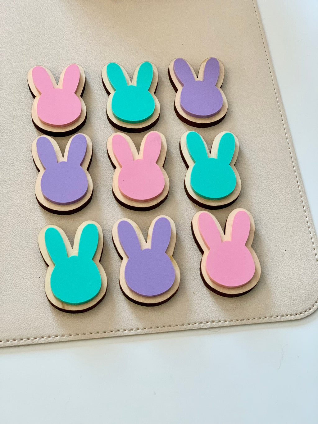 Set of pastel pink, purple, and teal wooden bunny-shaped cookies on beige surface arranged in a grid pattern