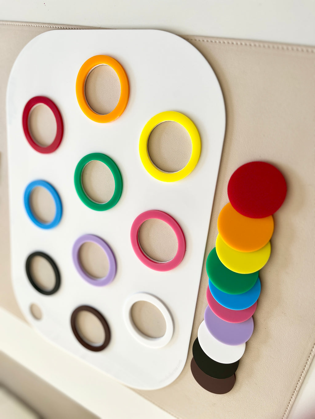 White board with colorful plastic rings arranged in rows and matching solid discs stacked beside it on a beige surface