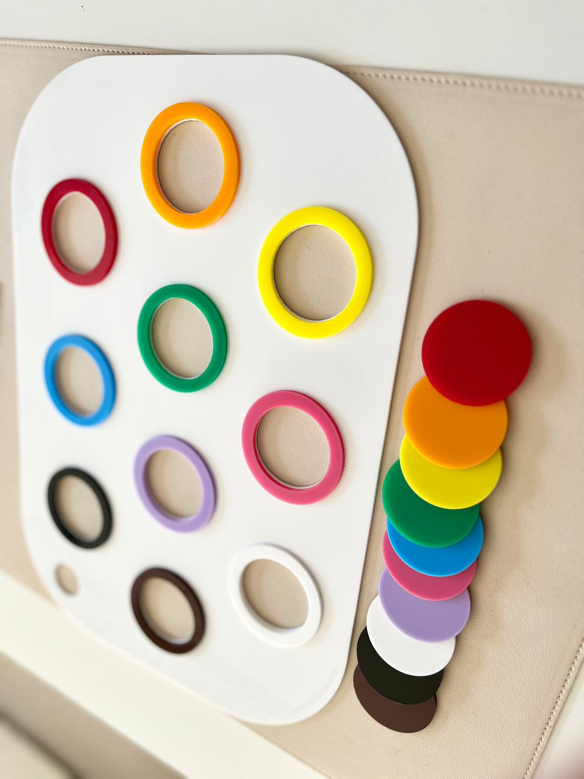 White board with colorful plastic rings arranged in rows and matching solid discs stacked beside it on a beige surface