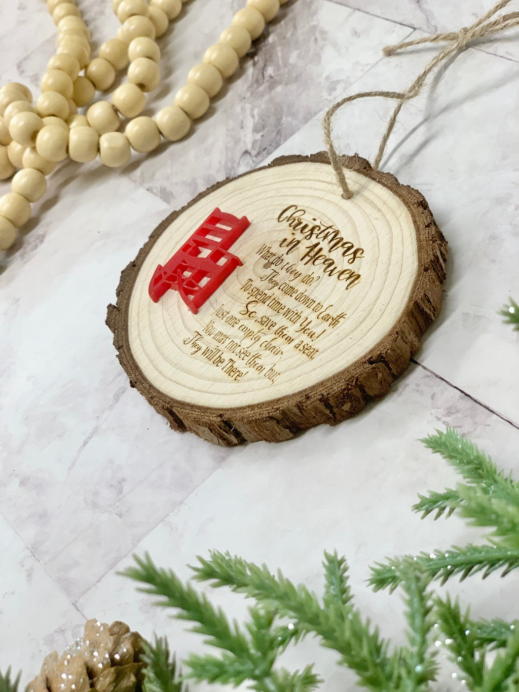 Wood slice memorial poem Christmas ornament with red chair decoration on marble surface with beads and greenery nearby