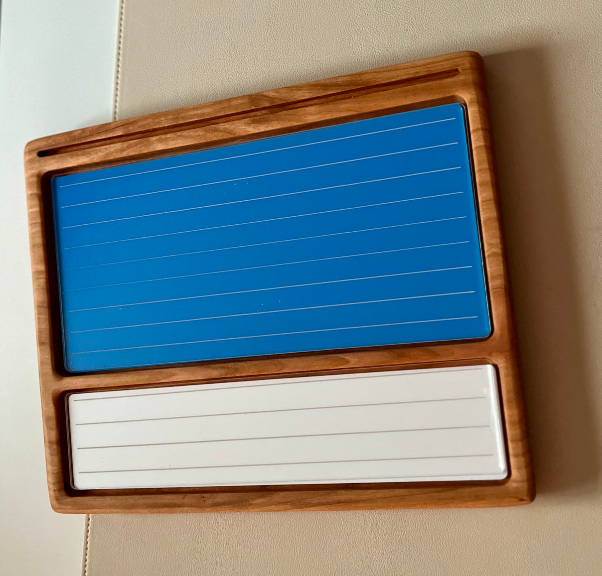 Smaller wooden multipurpose sensory tray with two dry erase inserts, one blue and one white with lined guides on beige surface