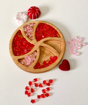 Round wooden tray with red and pink acrylic gems and felt heart and peppermint shapes on white surface