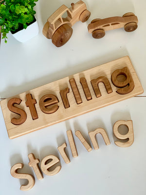 Personalized hardwood name puzzle with mixed wood letters spelling Sterling and two wooden toy cars on white surface