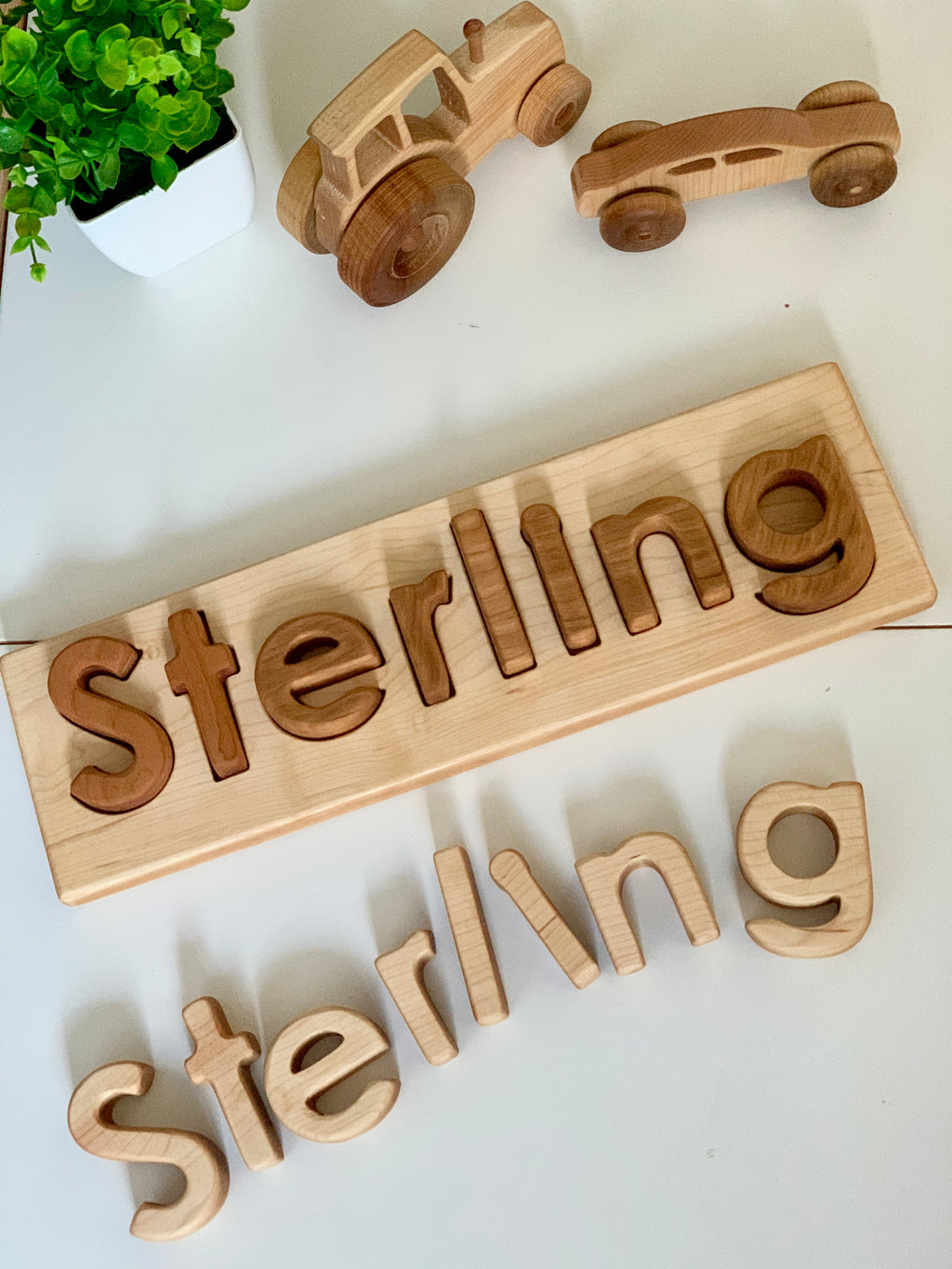 Personalized hardwood name puzzle with mixed wood letters spelling Sterling and two wooden toy cars on white surface