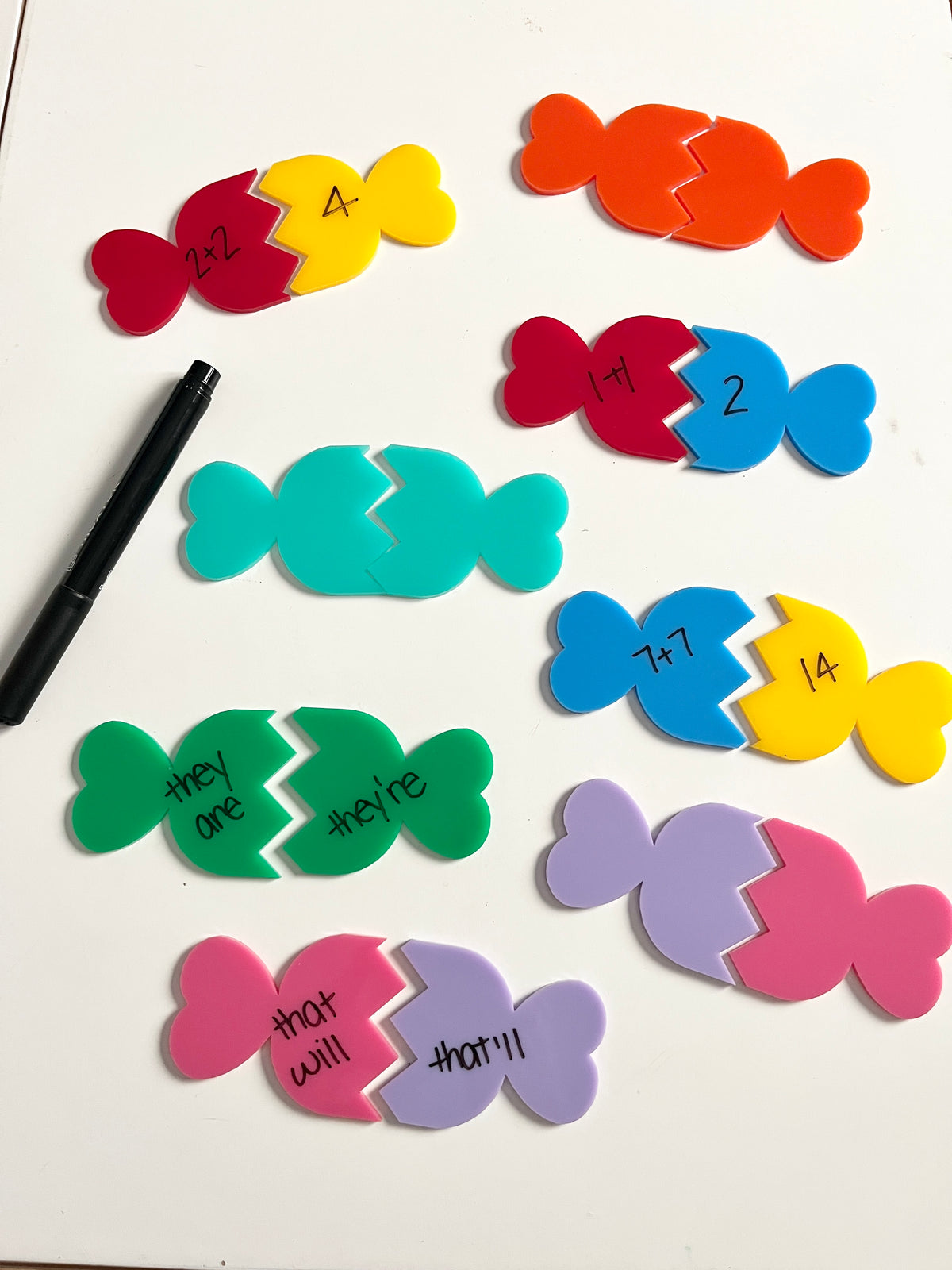 Little Dry Erasables - 2 Part Candies featuring colorful interlocking candy-shaped pieces with handwritten math equations and contractions, accompanied by a black dry-erase marker, handcrafted homeschool education resources.
