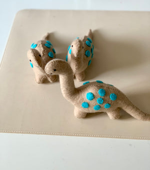 Set of three beige felt dinosaur toys with bright blue felt spots on a neutral surface