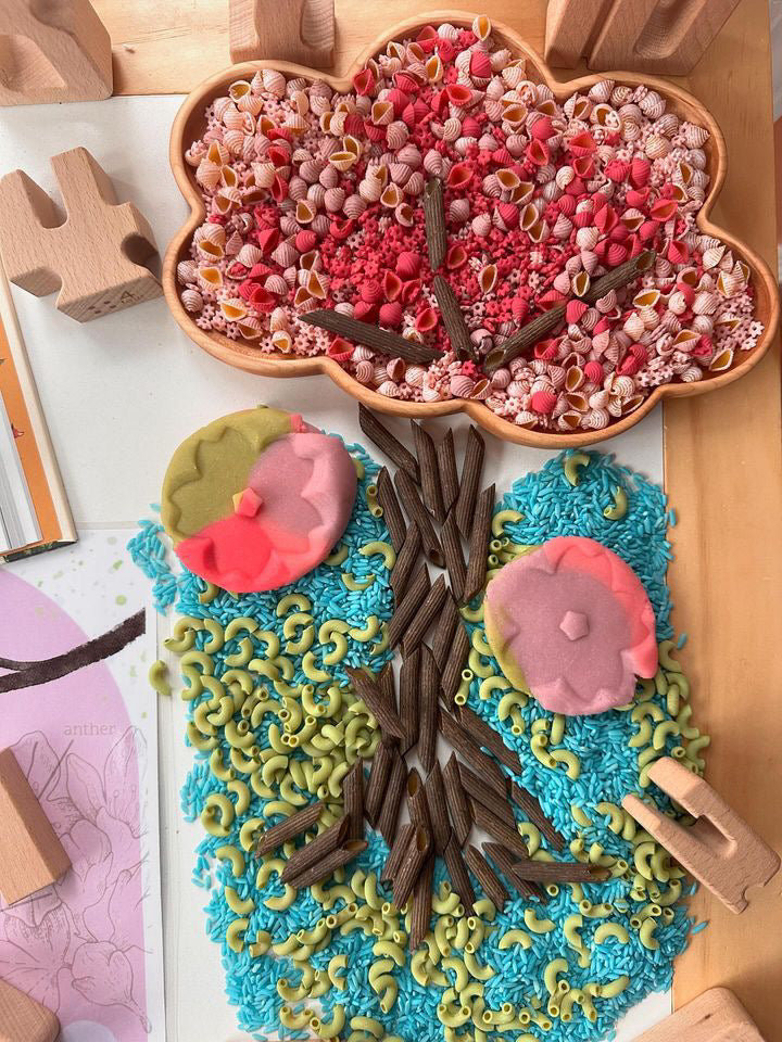 Cloud-shaped wooden sensory tray filled with colored pasta, seeds, and felt shapes on wooden surface with blocks