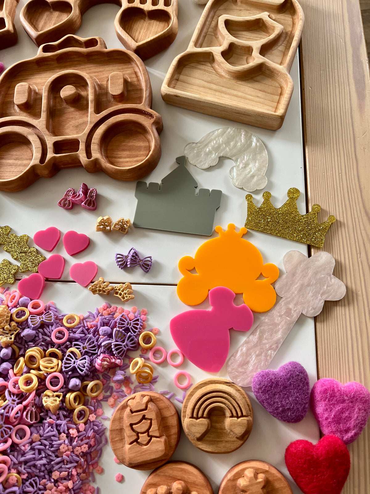 Assorted wooden trays, colorful plastic shapes, and textured sensory pieces arranged on a light surface near wood grain table edge