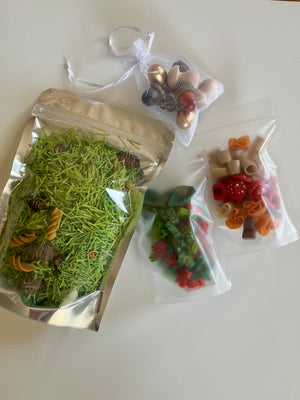 Assorted colorful pasta shapes and green rice in clear and metallic resealable bags on a white surface