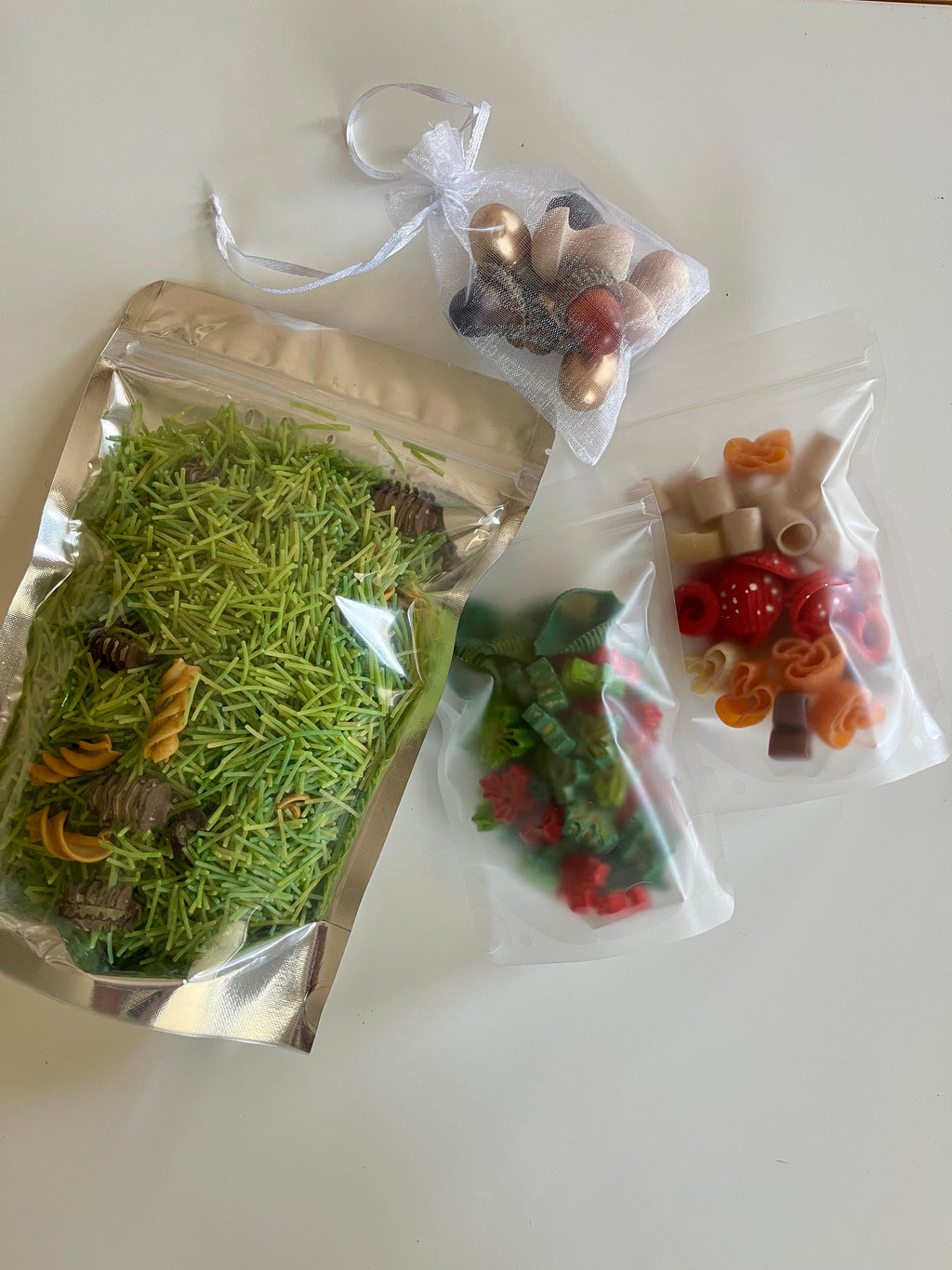 Assorted colorful pasta shapes and green rice in clear and metallic resealable bags on a white surface