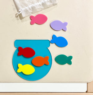 Colorful fish-shaped puzzle pieces with a blue fishbowl on a beige surface next to a white drawstring bag