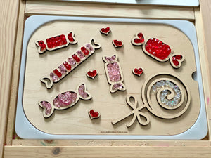 Wooden candy-shaped trays filled with red, pink, and clear acrylic gems arranged on a light wooden board