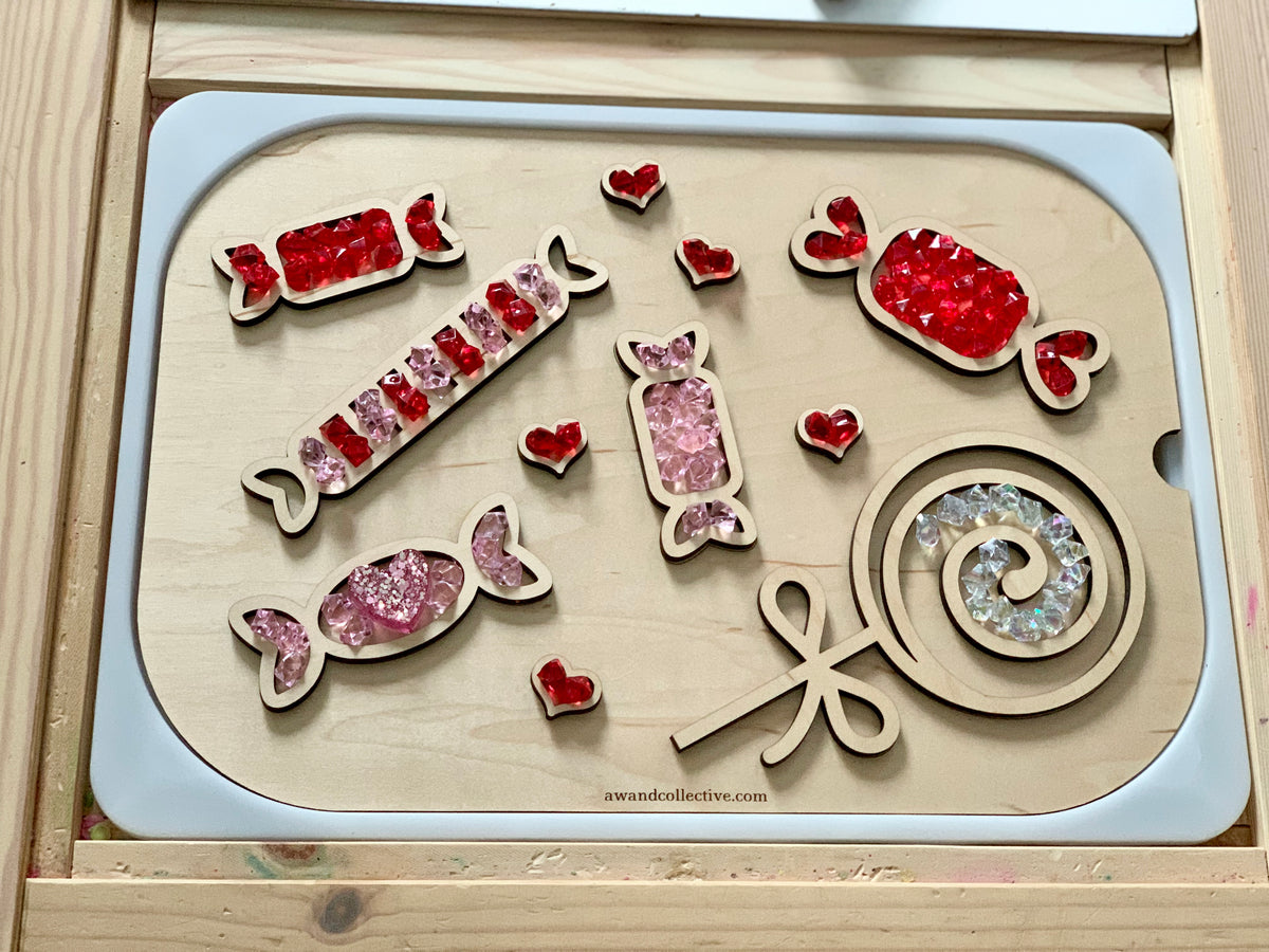 Wooden candy-shaped trays filled with red, pink, and clear acrylic gems arranged on a light wooden board
