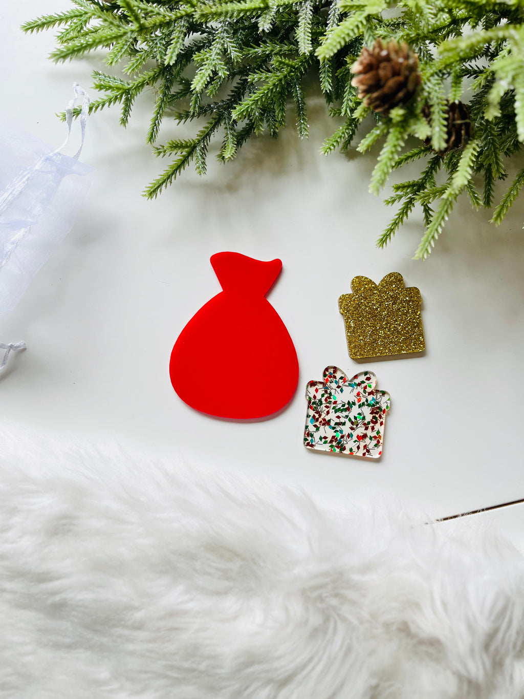 Red flat Santa sack cutout alongside two gift-shaped tokens, one gold glitter and one with red and green festive confetti, on white surface