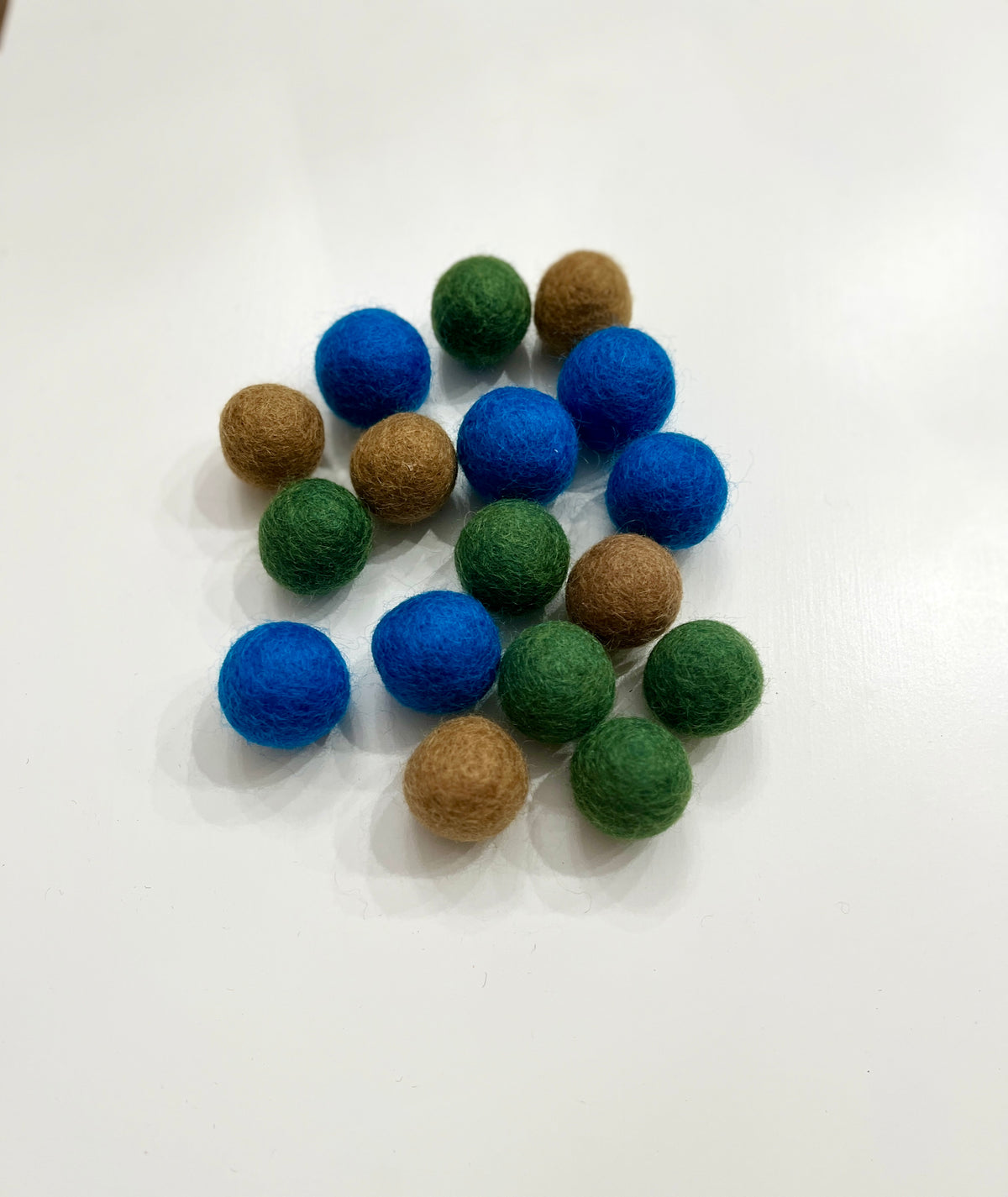 Collection of small felt balls in blue, green, and brown scattered on a white background surface