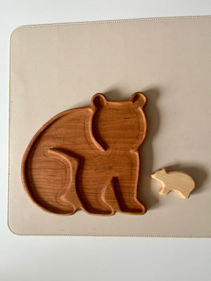 Two wooden bear-shaped objects, one a carved tray and the other a small solid figure on a light surface