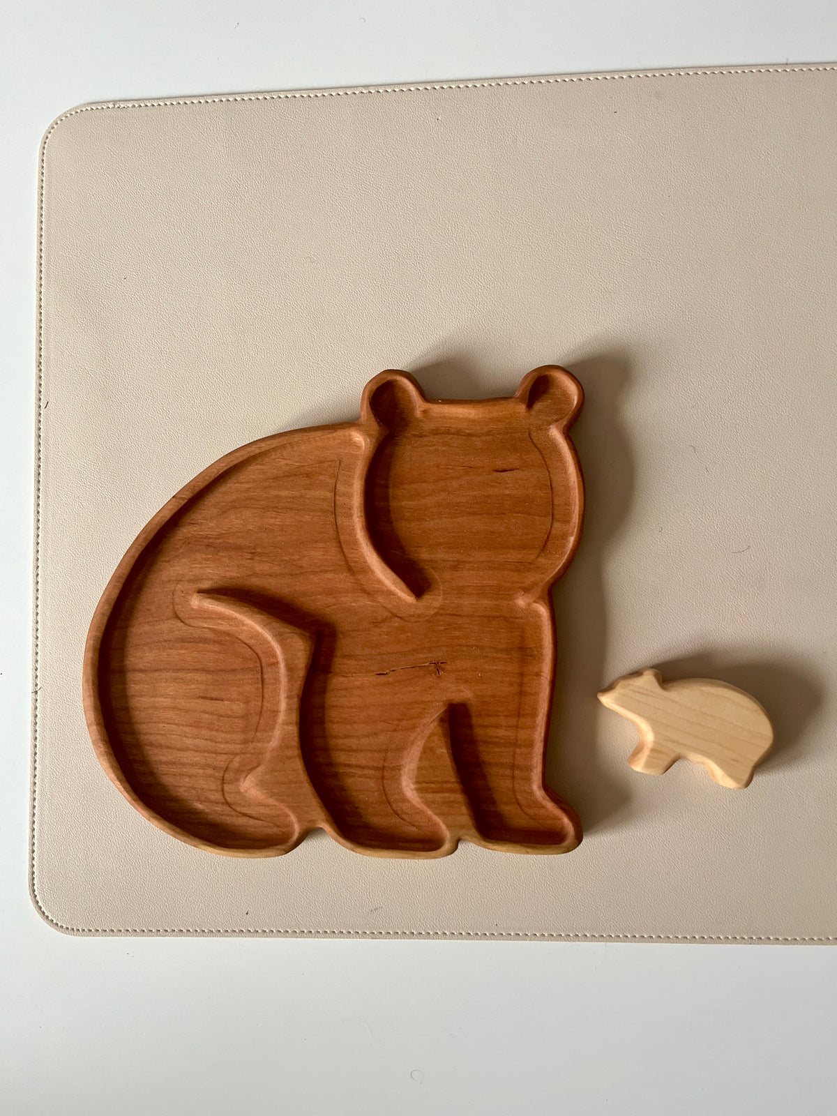 Two wooden bear-shaped objects, one a carved tray and the other a small solid figure on a light surface