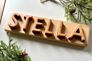 Personalized hardwood name puzzle with uppercase wooden letters spelling STELLA on natural wood base with pine accents