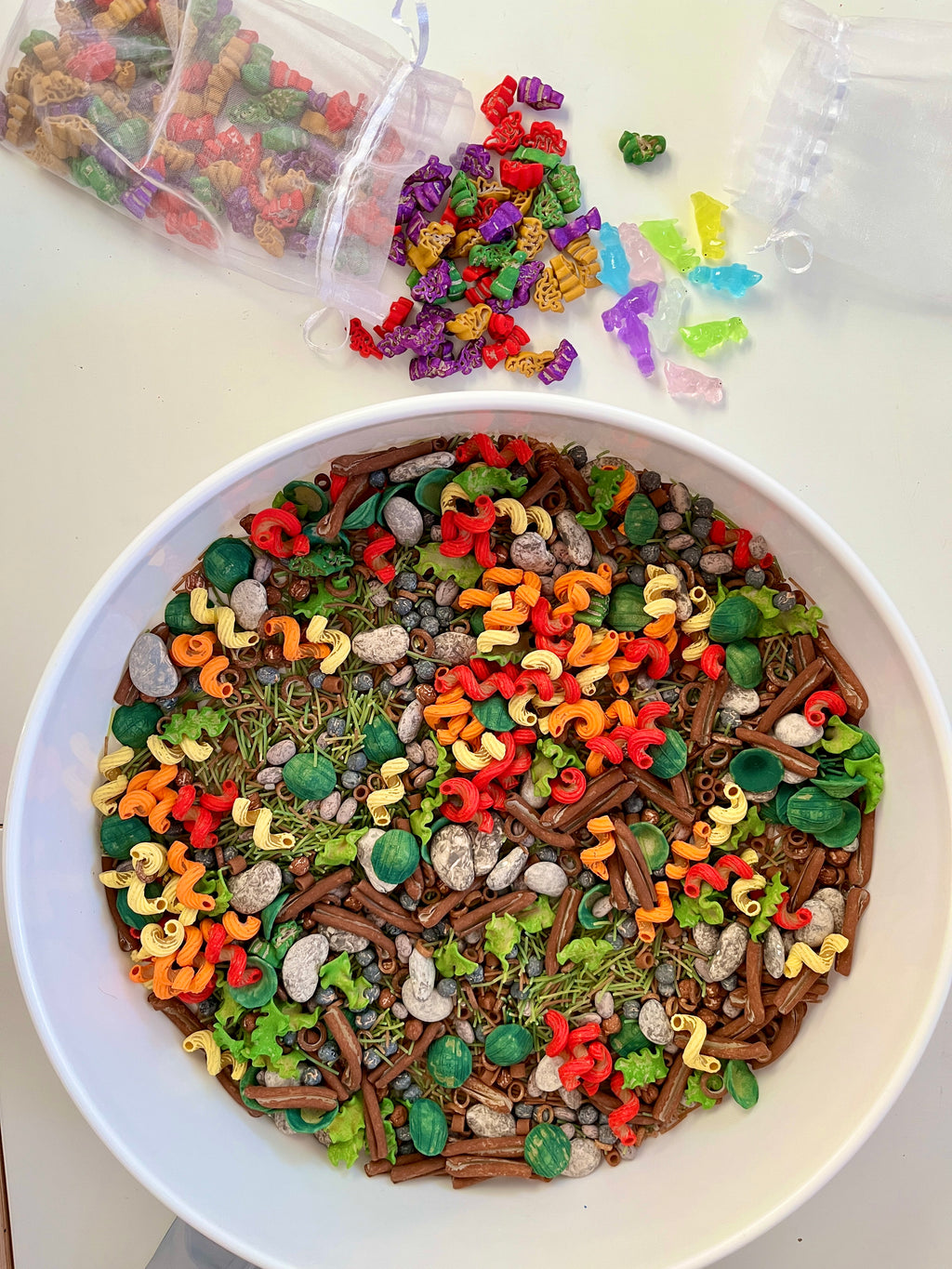 White bowl filled with colorful spiral pasta shapes, green sprouts, beans, and brown sticks on a white surface