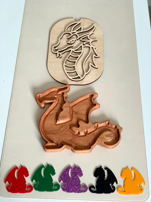 Wooden dragon head stencil above carved wooden dragon tray with red, green, purple, black, and yellow dragon-shaped pieces below