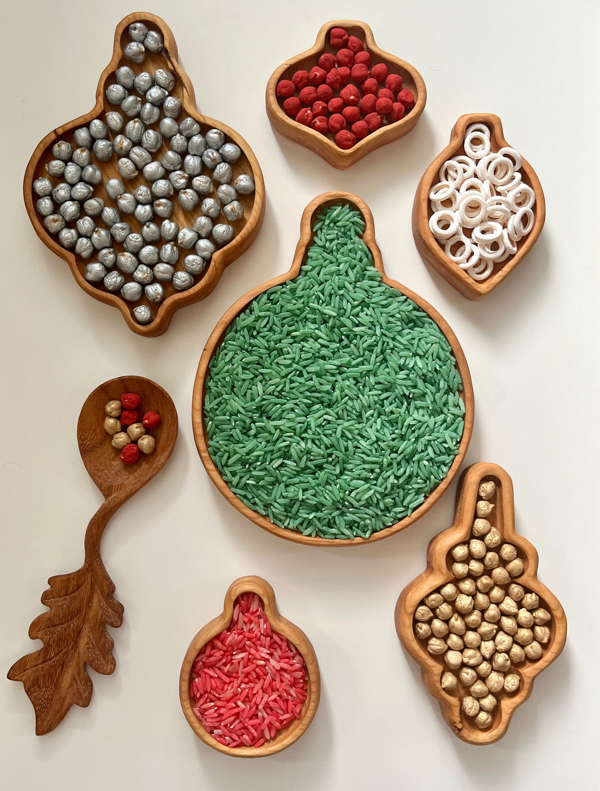 Set of wooden bowls shaped like gourds and leaves filled with colored rice, wooden beads, and rings on a white surface