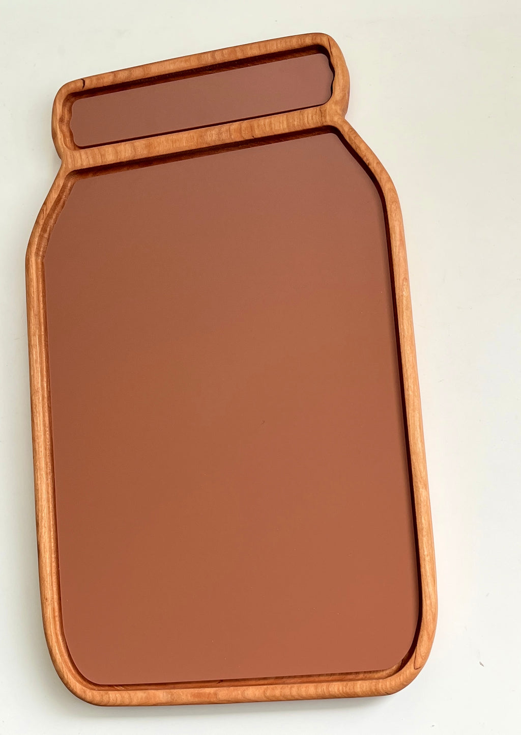 Wooden tray shaped like a jar with smooth edges and a solid muted terracotta-colored surface inside the frame