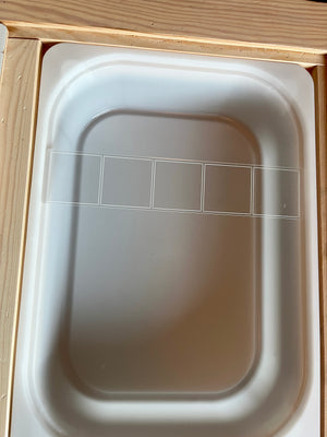 White rectangular tray with five outlined square sections on a light wooden surface background