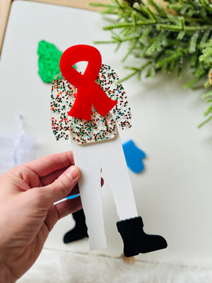 Hand holding white acrylic figure with floral top, black boots, and large red awareness ribbon cutout on decorative background