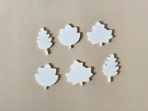 Six white leaf-shaped cutouts in different styles arranged on a beige surface