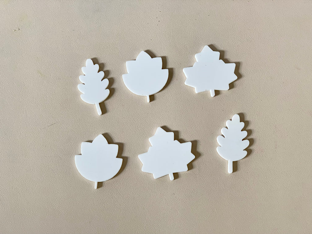 Six white leaf-shaped cutouts in different styles arranged on a beige surface