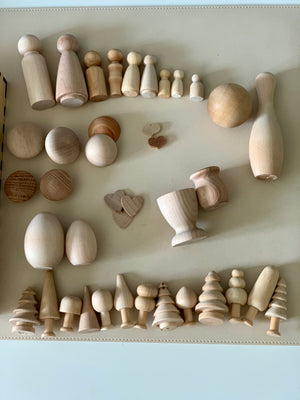 Assortment of unfinished natural wood shapes including peg dolls, spheres, trees, and small vessels on a light surface