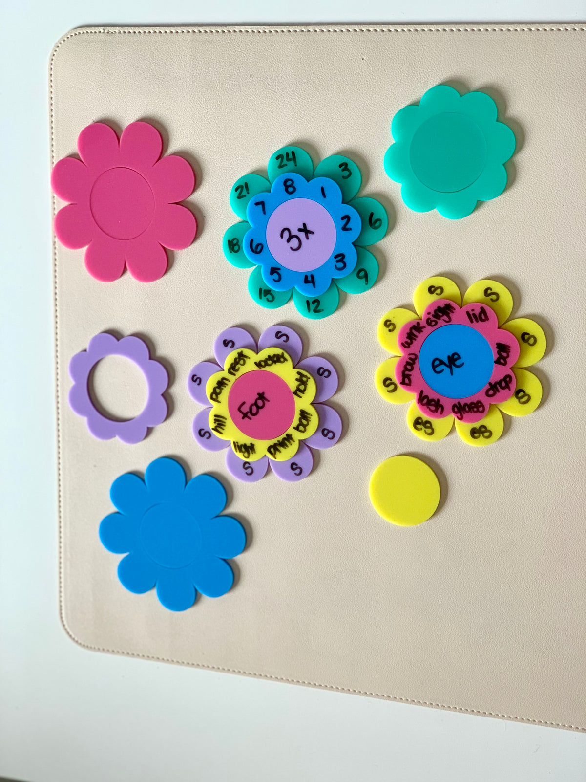 Colorful flower-shaped educational disks with numbers, words, and blank pieces arranged on a beige surface