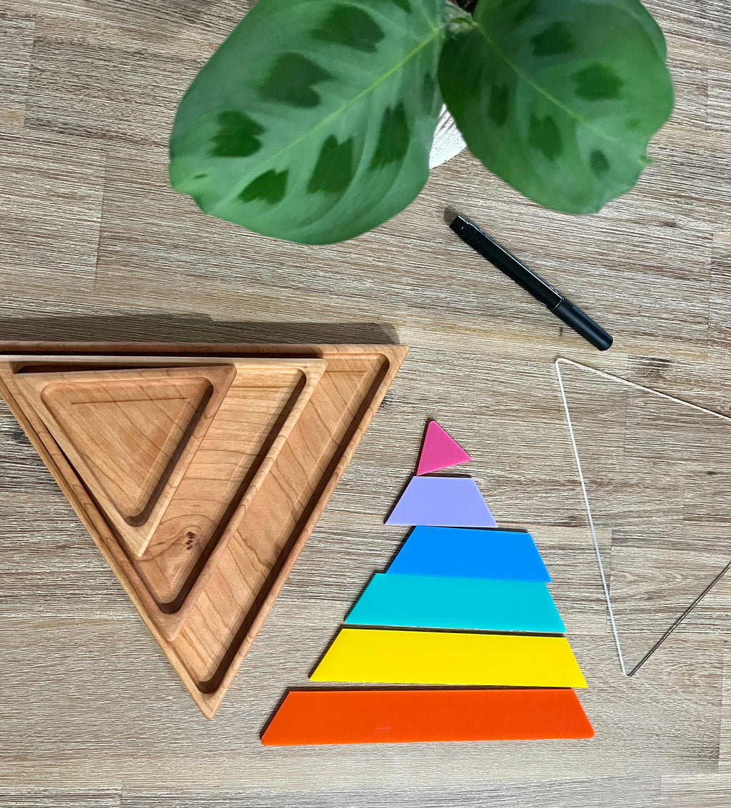 Nesting Triangle Pyramid Wooden Sensory Trays displayed with colorful layered wooden pieces arranged in size order beside natural wood trays on a table with a pen and green leaf, handcrafted homeschool education resources.