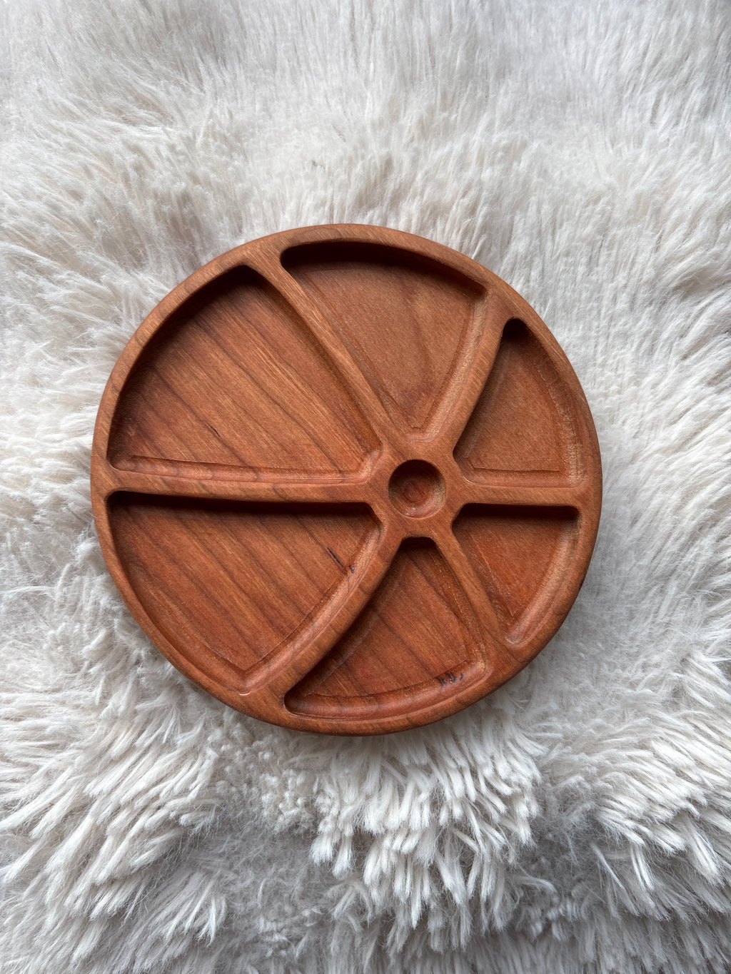 Round wooden tray with five curved compartments on a textured white fur surface