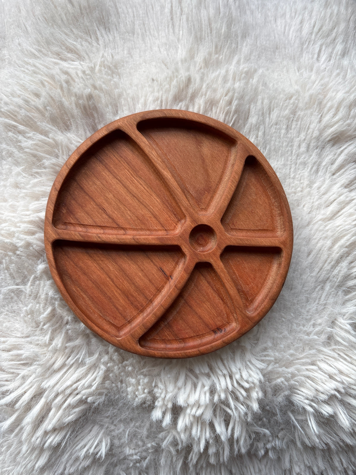 Round wooden tray with five curved compartments on a textured white fur surface