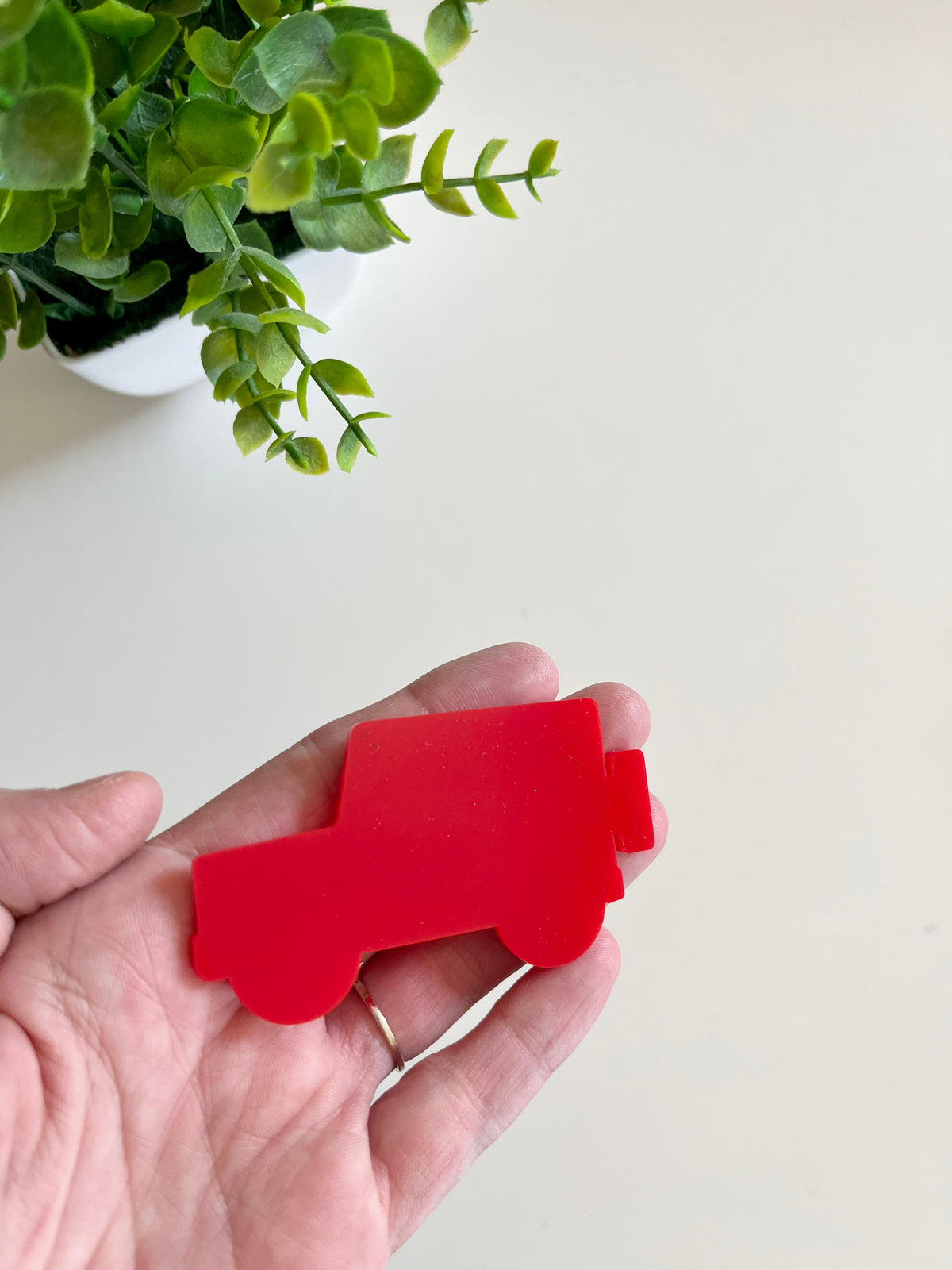 Person holding a smooth red car-shaped cutout with a green potted plant in the background on a light surface